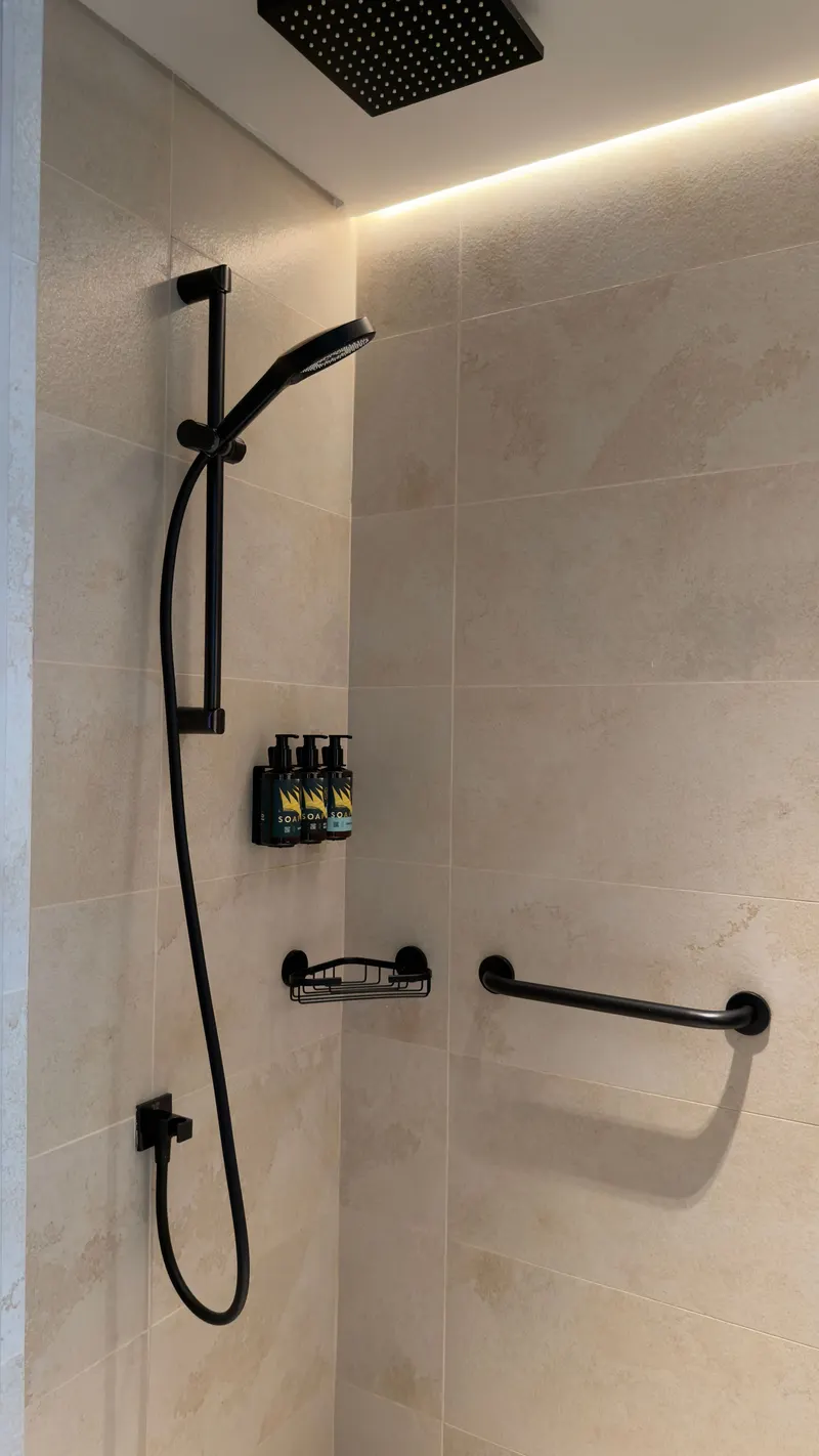 Dusche mit beigen Großformatfliesen, schwarzer Armatur und Haltegriff