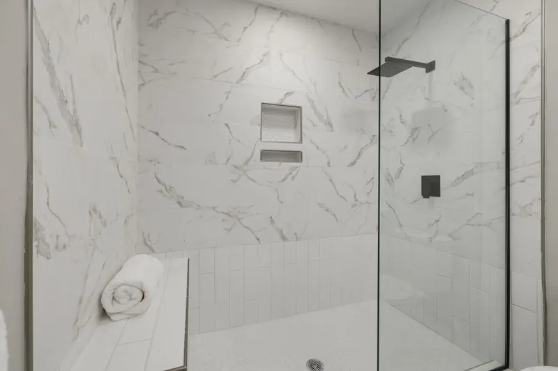 Dusche hinter Glas mit Wandfliesen in Marmoroptik, eingefliester Nische und Sitzbank