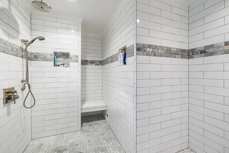 Weiß geflieste Dusche mit grauem Steinband, Sitzbank und Sechseck-Mosaik am Boden