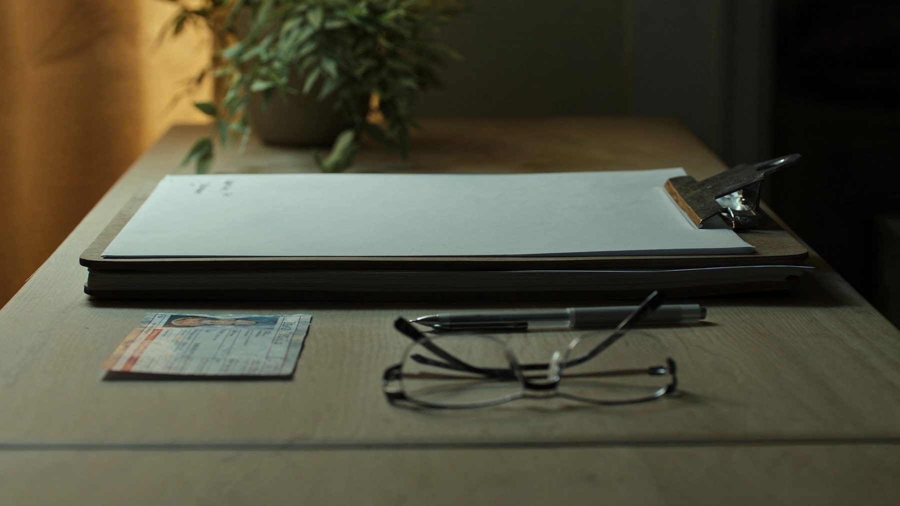 Klemmbrett mit leerem Blatt, Lesebrille und Stift auf einem Schreibtisch