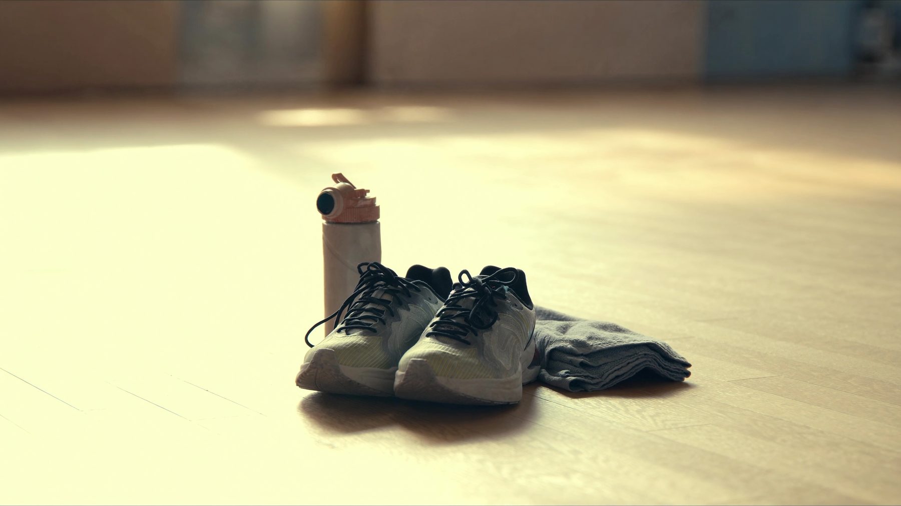 Laufschuhe, Trinkflasche und Handtuch auf heller Trainingsfläche
